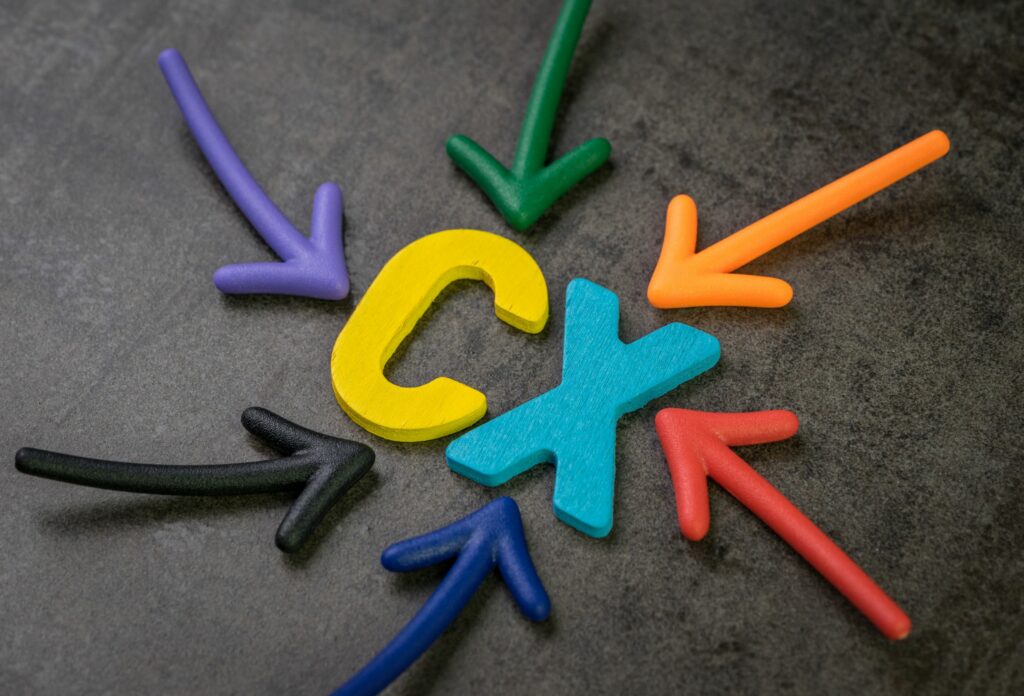 Bunte Pfeile zeigen auf die Holzbuchstaben C und X auf dunklem Hintergrund und symbolisieren das Konzept der Continuous Experience (CX) in der Kundeninteraktion. - RUF Beratung - Ihre Contact Center Berater