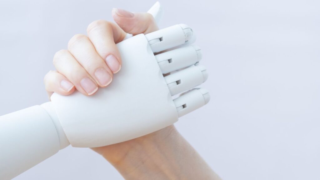 Zwei Hände die sich die Hand geben. Die eine Hand ist eine MEnschenhand. Die andere die eines Roboters.